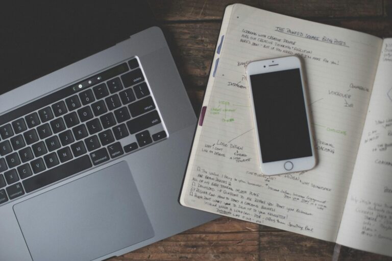Aerial view of a desk featuring a laptop, smartphone, and open notebook with handwritten notes.